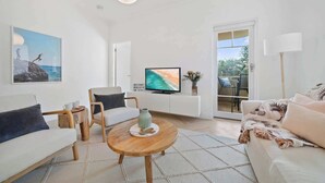 Una sala de estar moderna con sofá, sillón, mesa de centro, televisor y vistas a través de un ventanal.