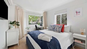 Una habitación de hotel moderna con una cama grande, un escritorio y una ventana con vistas a zonas verdes.