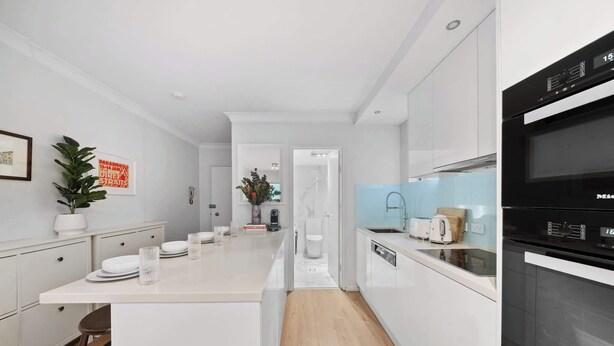 Una cocina moderna con armarios blancos, una isla central, horno empotrado y cafetera.