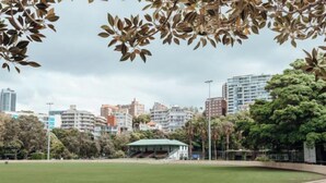 Un parque con un césped verde, una valla de madera y edificios al fondo.