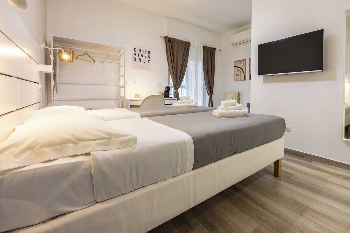 A modern hotel room with two beds, a flat-screen TV, and a mirror.