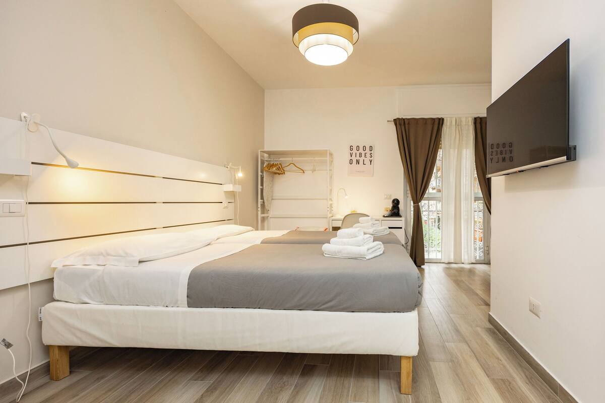 A modern hotel room with a large bed, bedside tables, a TV, and a view of the outdoors.