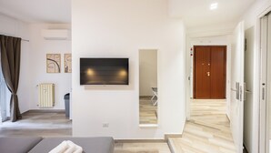 Ett modernt hotellrum med en säng, en platt-TV som är monterad på väggen, ett element och en dörr av trä.