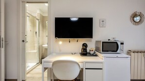 Ett modernt, vitt rum med ett skrivbord, en tv som är monterad ovanför skrivbordet, en mikrovågsugn och ett element.