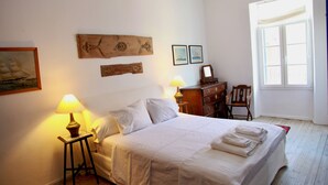 Un dormitorio ordenado con cama, lámparas de noche, cómoda y ventana con luz natural.