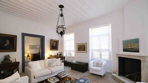 Amplia sala de estar con un sofá blanco, una mesa de centro con libros, una chimenea y ventanas grandes que dejan entrar luz natural.