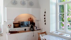 Una cocina con armarios blancos, una mesa de comedor blanca con sillas, una lámpara colgante y una ventana que ofrece vistas a follaje.