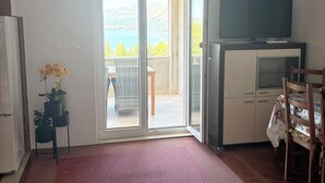 Een kamer met een groot raam, een flatscreen-televisie, een eethoek en een rood tapijt.