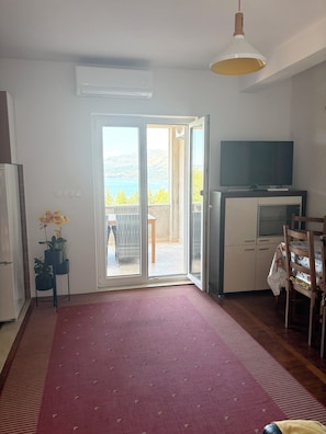 Ein Zimmer mit großem Fenster, einem Flachbildfernseher, einem Essbereich und einem roten Teppich.