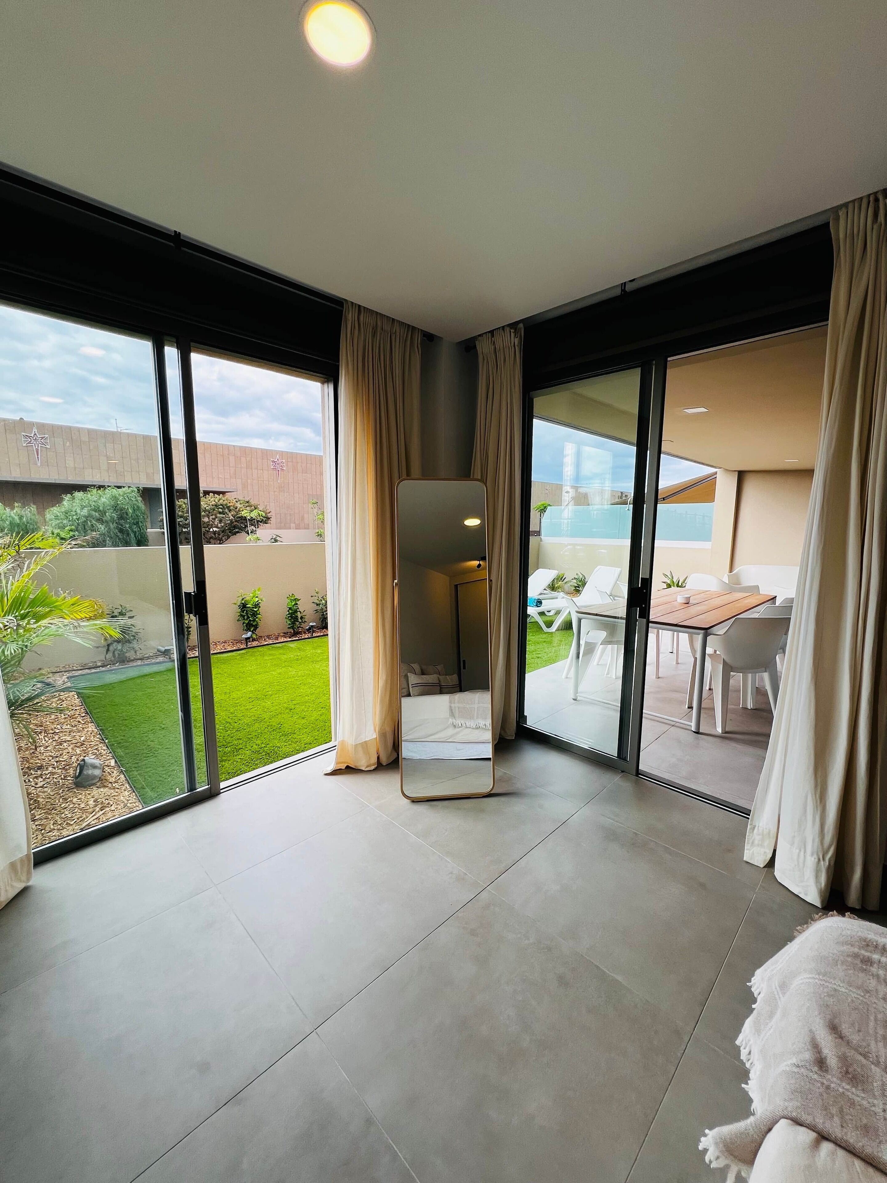 A modern hotel room with large sliding glass doors leading to a balcony, a flat-screen TV, and a small seating area with a table and chairs.