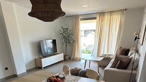 A modern living room with a dining area, featuring a wooden table, chairs, a TV, a sofa, and a plant.