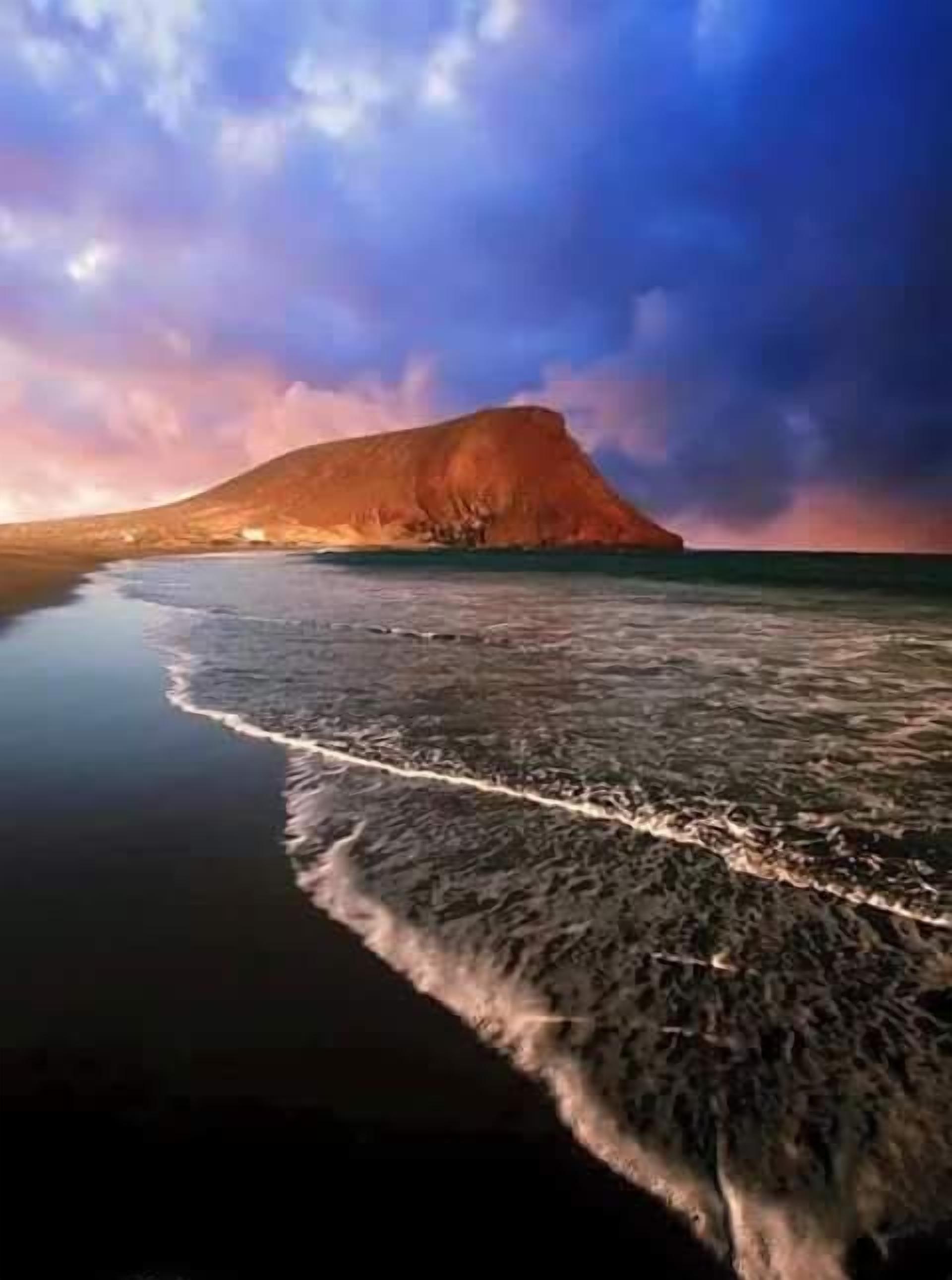 Ein Strand mit einem Berg im Hintergrund und ruhigem Wasser.
