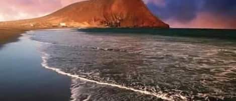 Ein Strand mit einem Berg im Hintergrund und ruhigem Wasser.