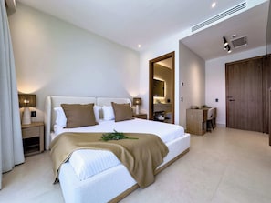 A modern bedroom with a large bed, bedside lamps, a wooden wardrobe, and a bathroom visible through an open door.