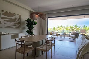 A modern living room with a dining area, large windows, and a view of palm trees.