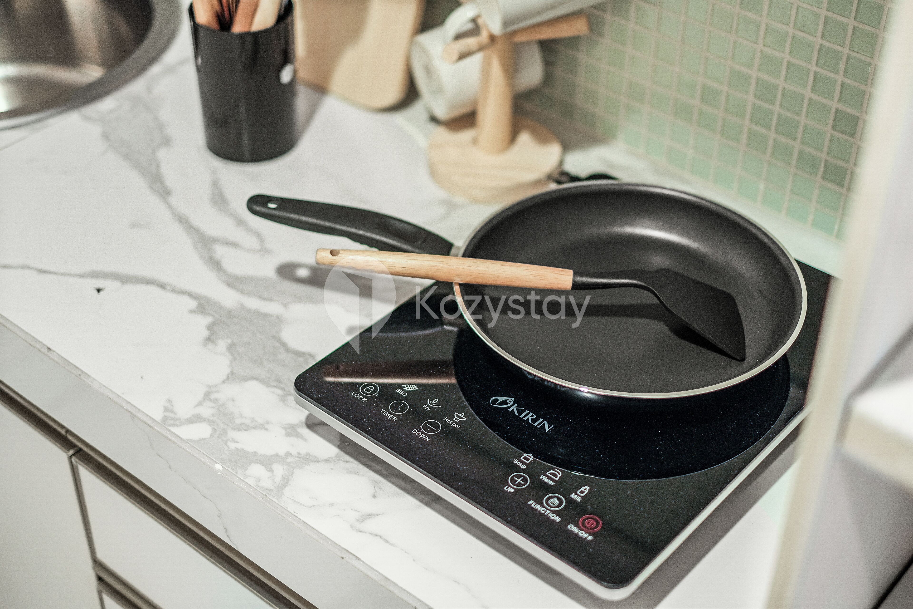 A kitchen with a black induction cooktop, a frying pan, and wooden utensils.