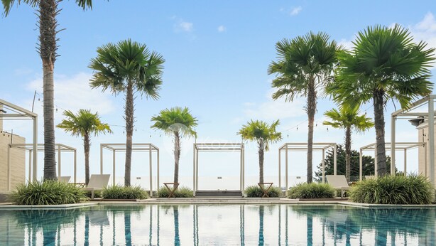 A pool area with palm trees, lounge chairs, and a clear sky. - Astrum by Kozystay - Ciumbuleuit (Bandung)