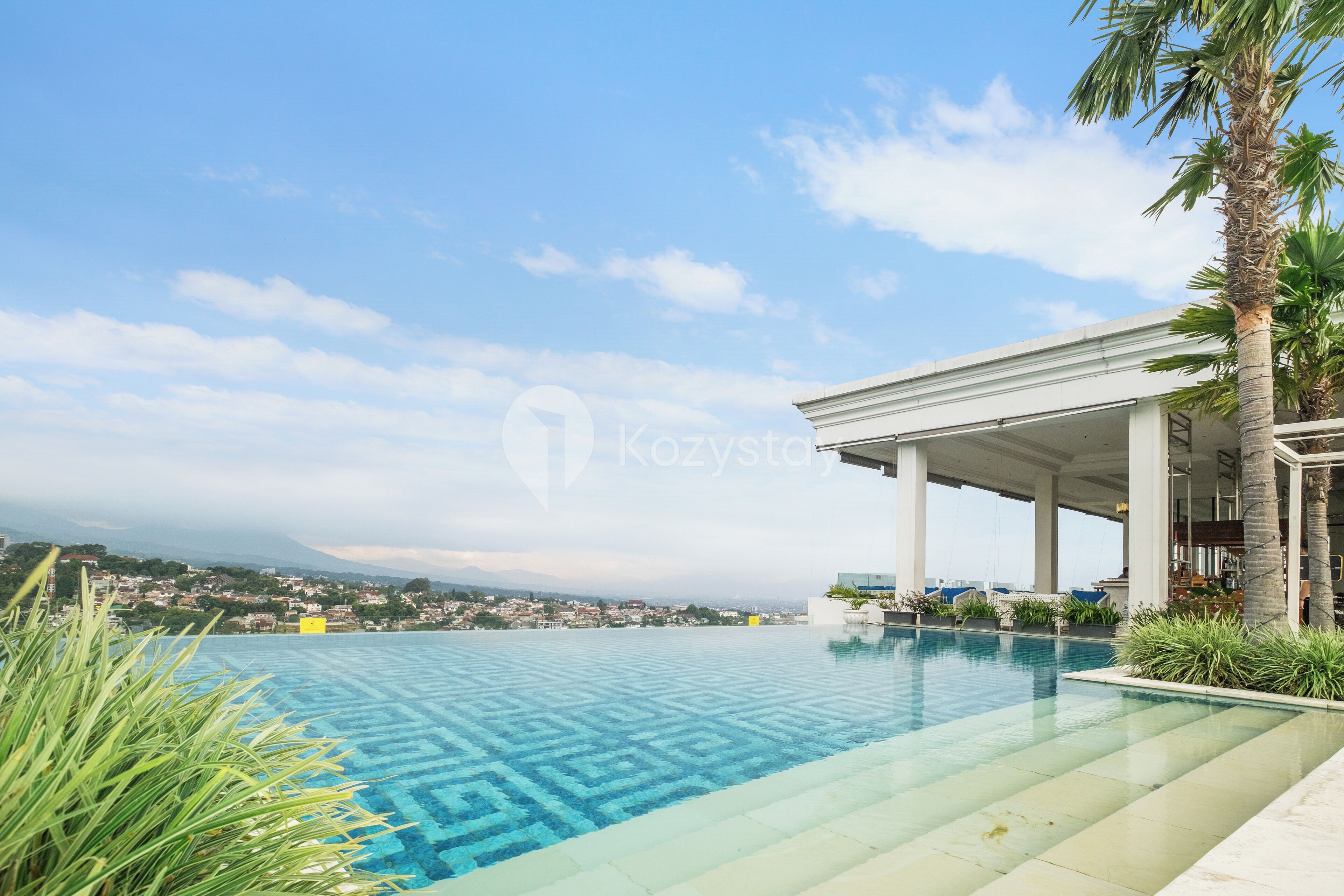 Piscina con un diseño geométrico, rodeada de vegetación y una zona cubierta con columnas.