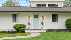 A single-story house with a light blue front door, two windows on the upper floor, and a small front yard with a pathway leading to the door.