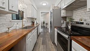 A modern kitchen with white cabinetry, a wooden countertop, a stainless steel refrigerator, and a black oven.