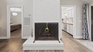 A modern living room with a fireplace, a dining area, and a kitchen visible through an open door.