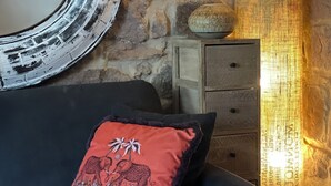 Una habitación con pared de piedra, un espejo redondo, una lámpara y un sofá con un cojín decorativo.