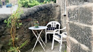 Un muro de piedra con una pequeña mesa, dos sillas, una planta en maceta y un letrero que indica una pendiente del 12%.