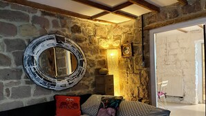 Un dormitorio con pared de piedra, un espejo redondo, una cama con ropa de cama estampada y techo de madera.