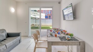 Una sala de estar moderna con un sofá gris, una mesa de comedor con sillas, un televisor de pantalla plana montado en la pared y un ventanal corredizo que da a un patio exterior.