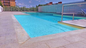Una piscina con plataforma de azulejos, un trampolín y una valla.