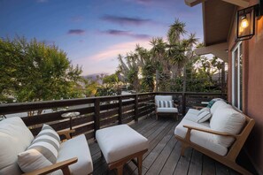 A deck with outdoor seating, a railing, and a view of trees and a building. - Walk to the Beach & Famous Sunset Cliffs | Hot Tub (San Diego)
