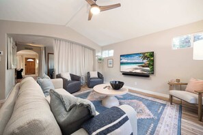 Un salon comprenant un canapé, des fauteuils, une table basse, un tableau et un ventilateur de plafond.