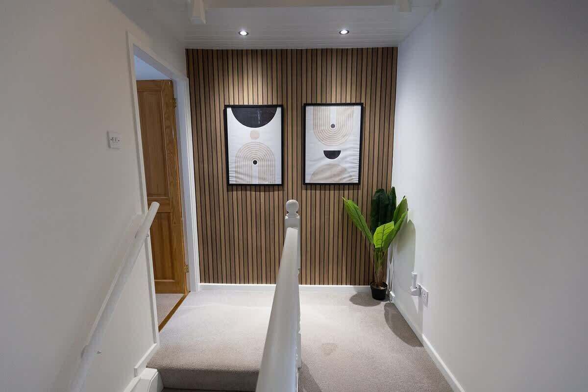 Un couloir avec un mur en bois, deux œuvres d’art abstraites encadrées, une plante en pot et un escalier blanc.