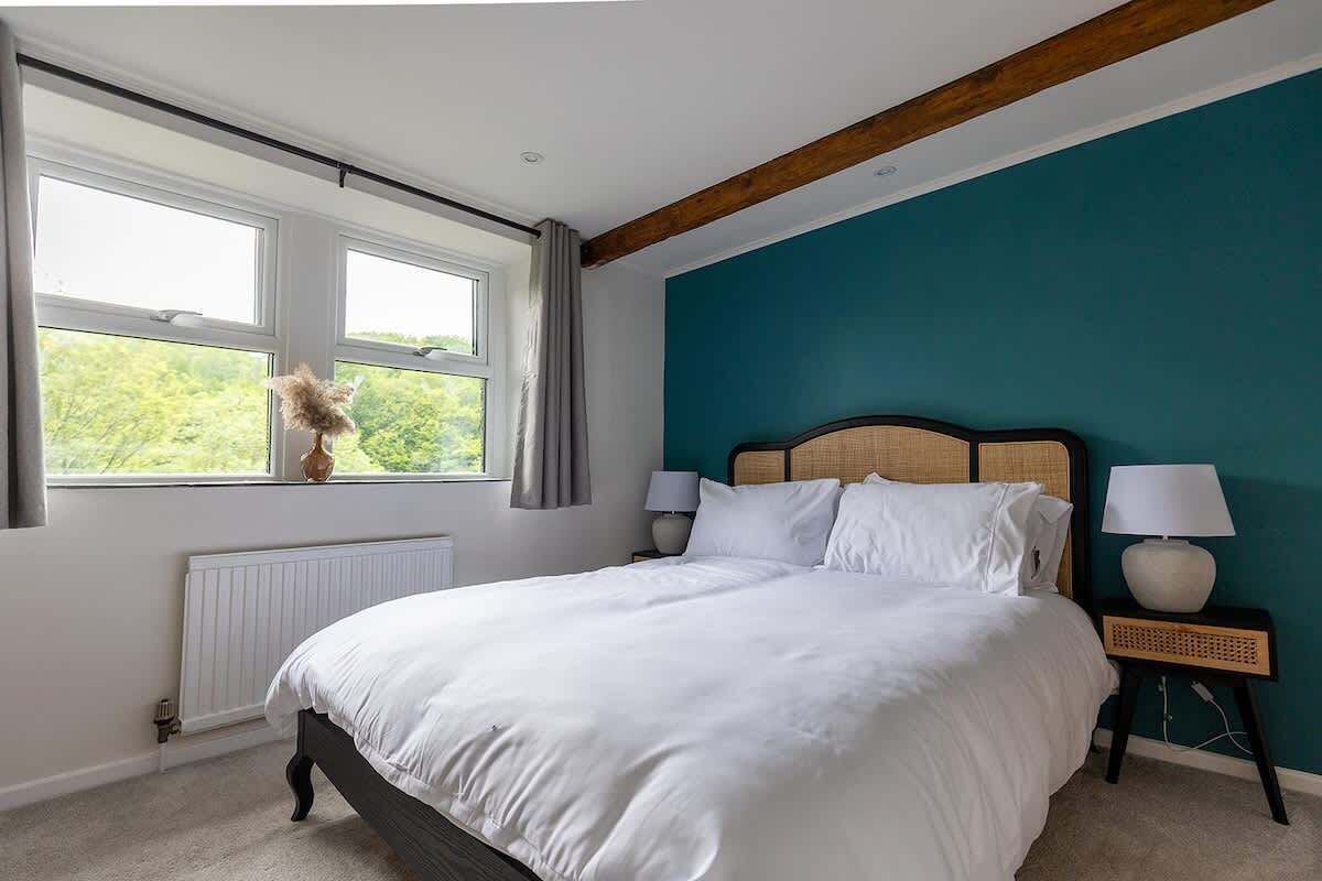 Ein Schlafzimmer mit Bett, Vorhängen am Fenster, Heizkörper, Kopfteil und Nachttischlampen.