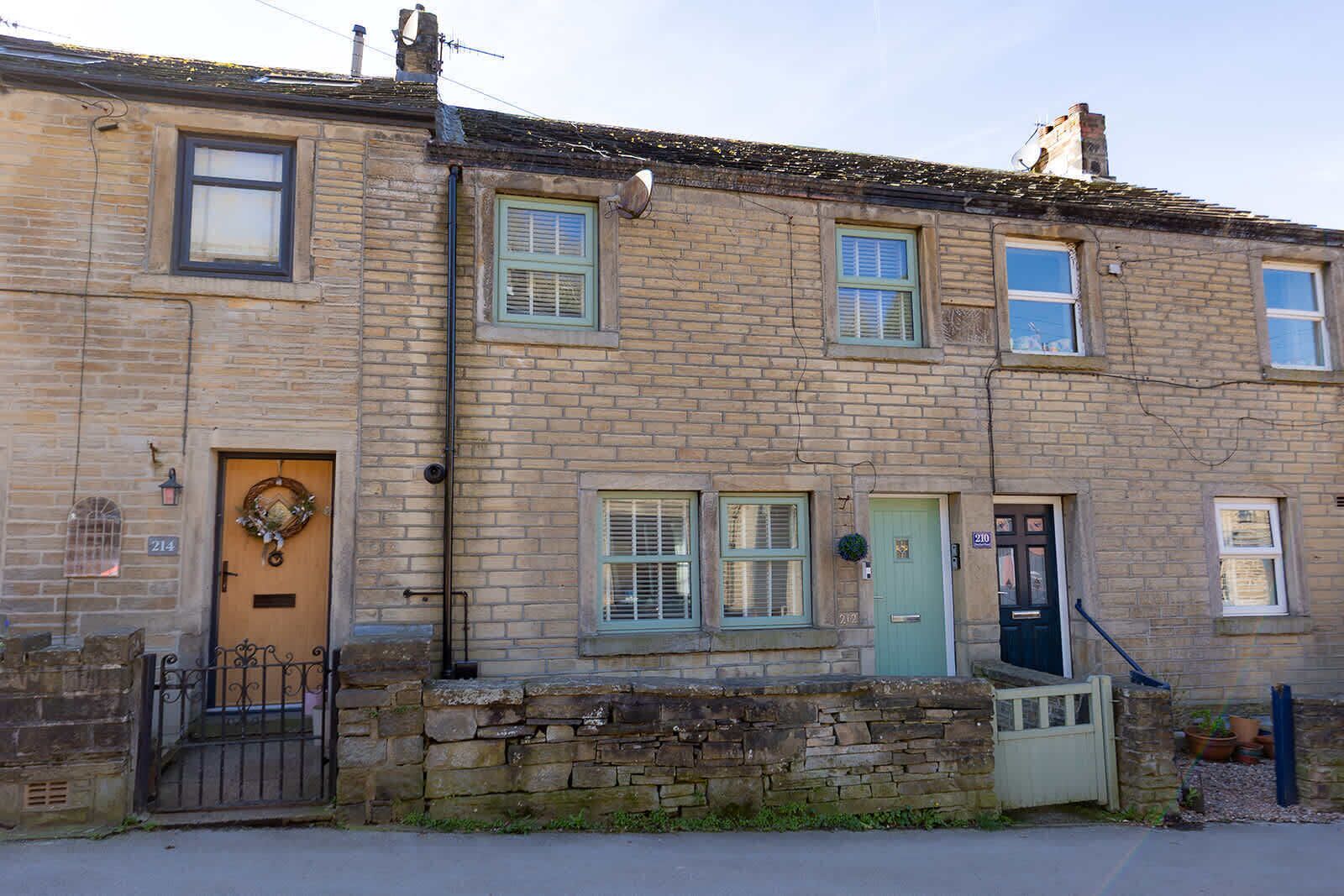 A two-story brick building with a stone wall entrance, numbered doors, and a small garden area.