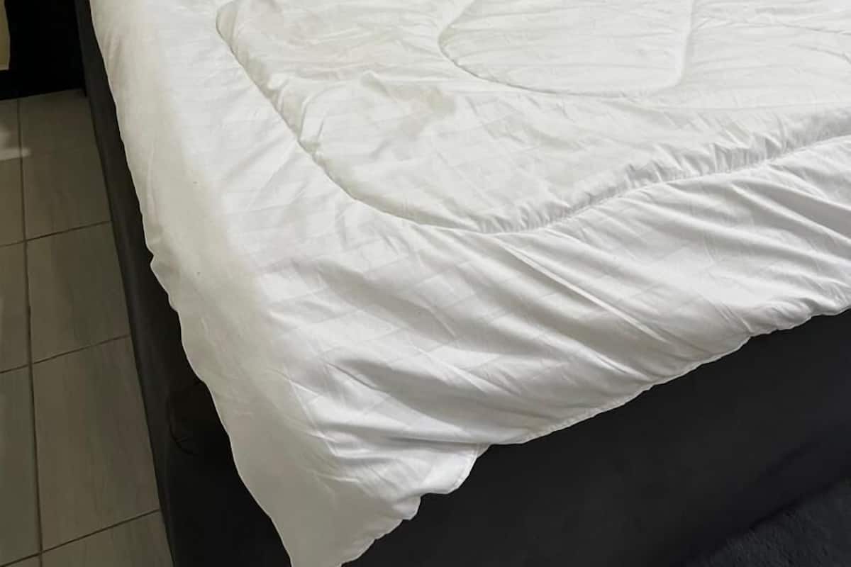 A neatly made bed with white linens and a dark headboard in a room with tiled flooring.