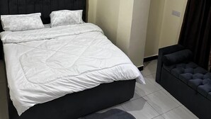A bedroom with a bed, a dark headboard, a dark sofa, and a light-colored wall. - Girrafe Apartments (Dar es Salaam)
