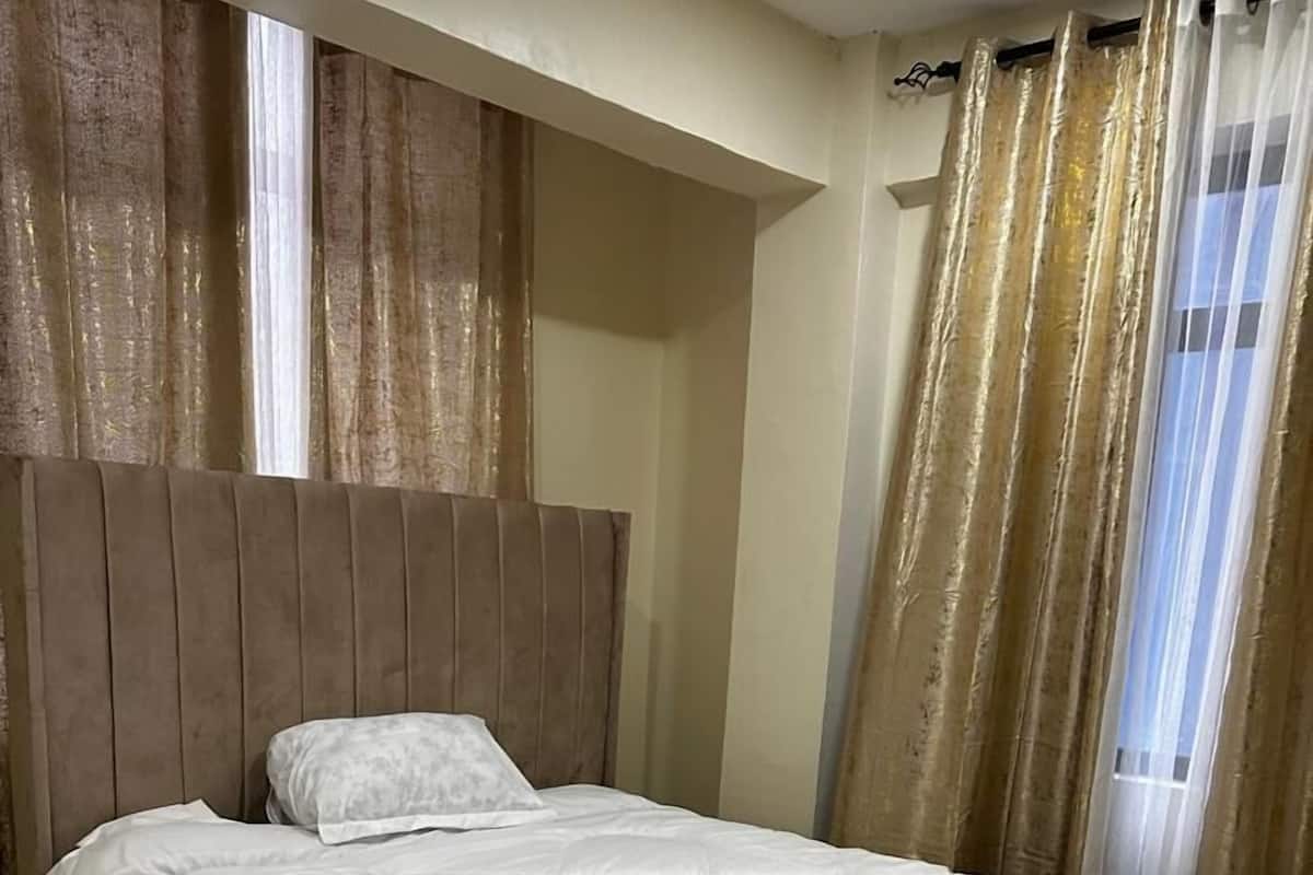 A single bed with a headboard, white bedding, and a patterned throw blanket.