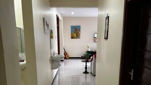 A hallway with a tiled floor, a door on the right, and a wall with a painting and a guitar. - Girrafe Apartments (Dar es Salaam)