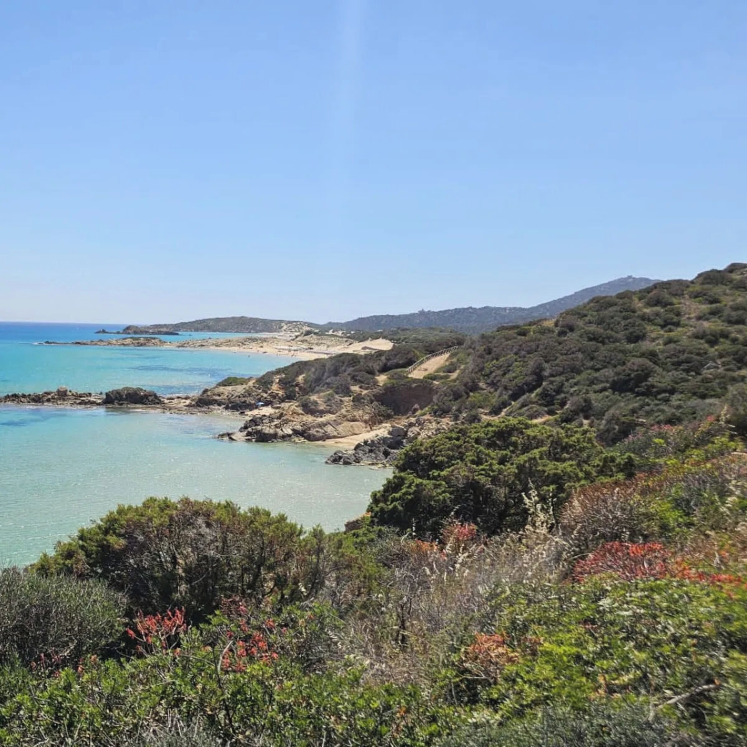 A coastal landscape with clear waters, rocky terrain, and dense vegetation.