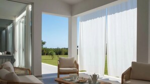 Una sala de estar moderna con un ventanal que da a un balcón, dos sofás, una mesa de centro con juego de té y vistas a un paisaje verde.