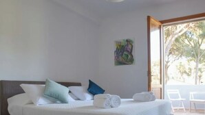 Un dormitorio con cama, almohadas, un cuadro y vistas a través de un ventanal.
