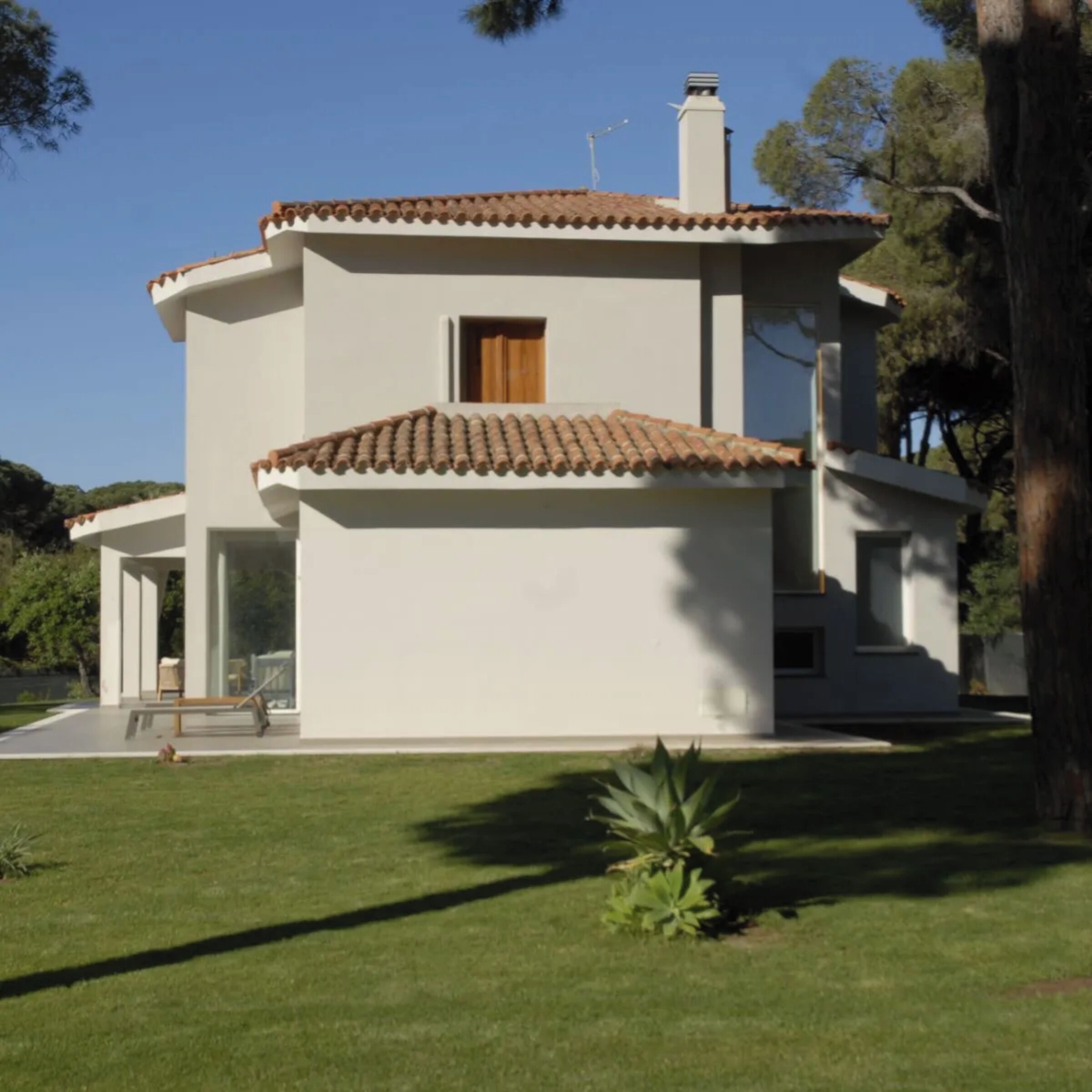 Une maison moderne à deux étages, avec un toit en tuiles, une petite fenêtre et une véranda couverte.