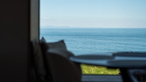 A view from a room with a window overlooking a body of water and distant landforms. - Peninsula Suites (Hellnar)