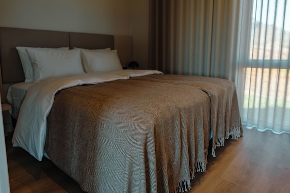A neatly made bed with a patterned bedspread and pillows, a wooden floor, and a window with curtains. - Peninsula Suites (Hellnar)