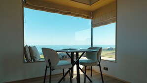 A dining area with a table and chairs, large windows with a view of the sea, and a wooden floor. - Peninsula Suites (Hellnar)