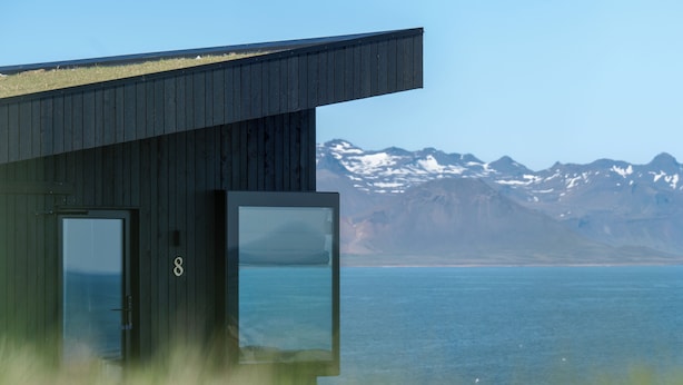 A modern building with a large glass door and a view of a mountain range and water. - Peninsula Suites (Hellnar)
