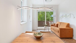 Ein modernes Wohnzimmer mit einem Holzesstisch, einer Couch und Blick auf einen Balkon mit Holzboden.