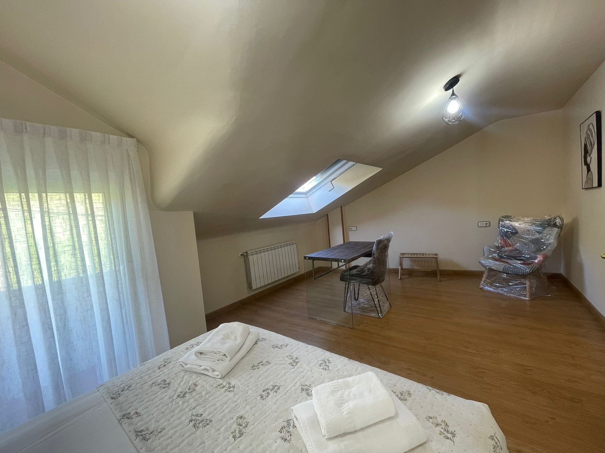 Ein Schlafzimmer mit einem Oberlicht, einem Bett mit floralem Überwurf, einem kleinen Tisch und einem Stuhl.