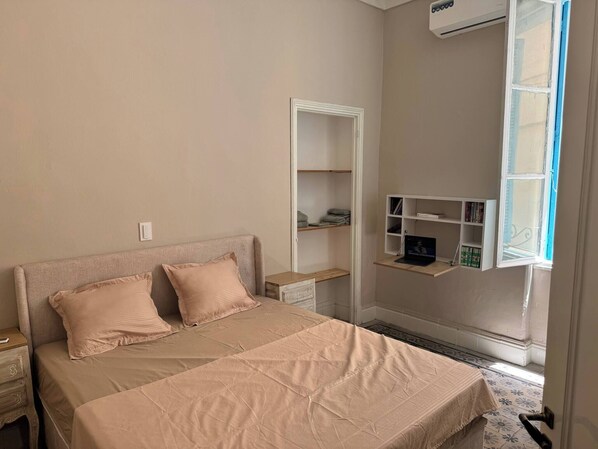 A bedroom with a bed, bedside tables, a wardrobe, and a window with shelves. - Cozy Luxury Apartment in the Heart of Tunis (Tunis)